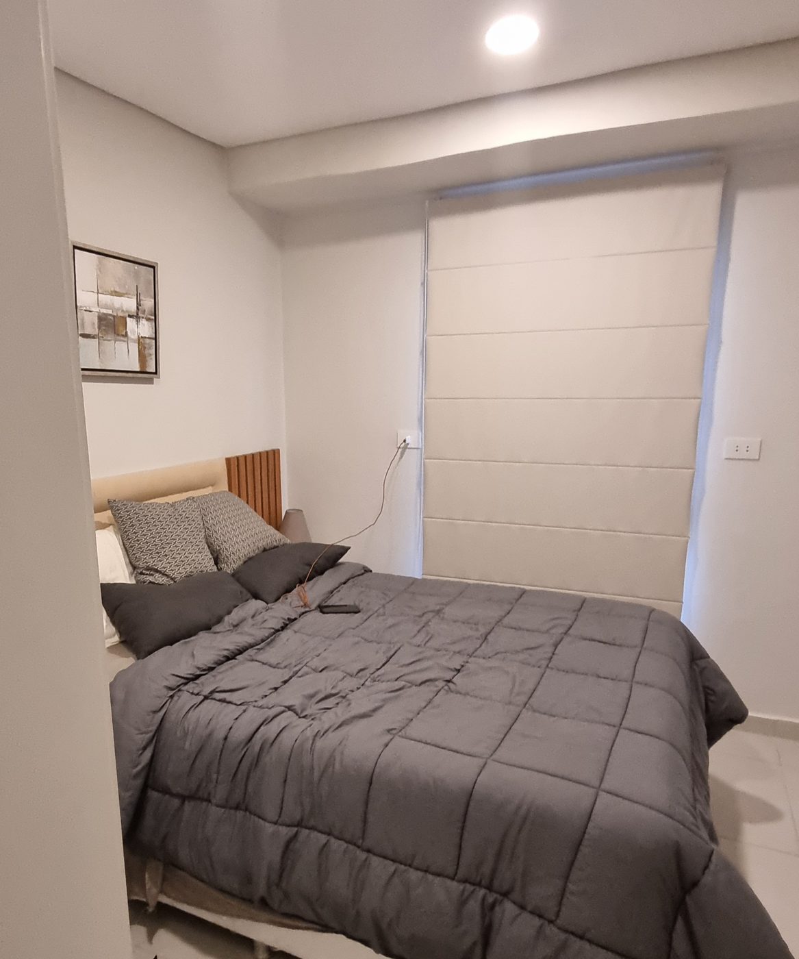 Helles Schlafzimmer mit Holzakzent am Bett und Faltrollo
